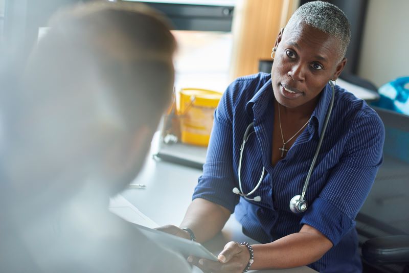 A health professional sat at a desk talk to another person who is facing away from the camera.