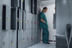 A health professional alone in a room leaning on some lockers.