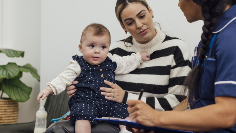 A mum holding a baby while talking to a health professional